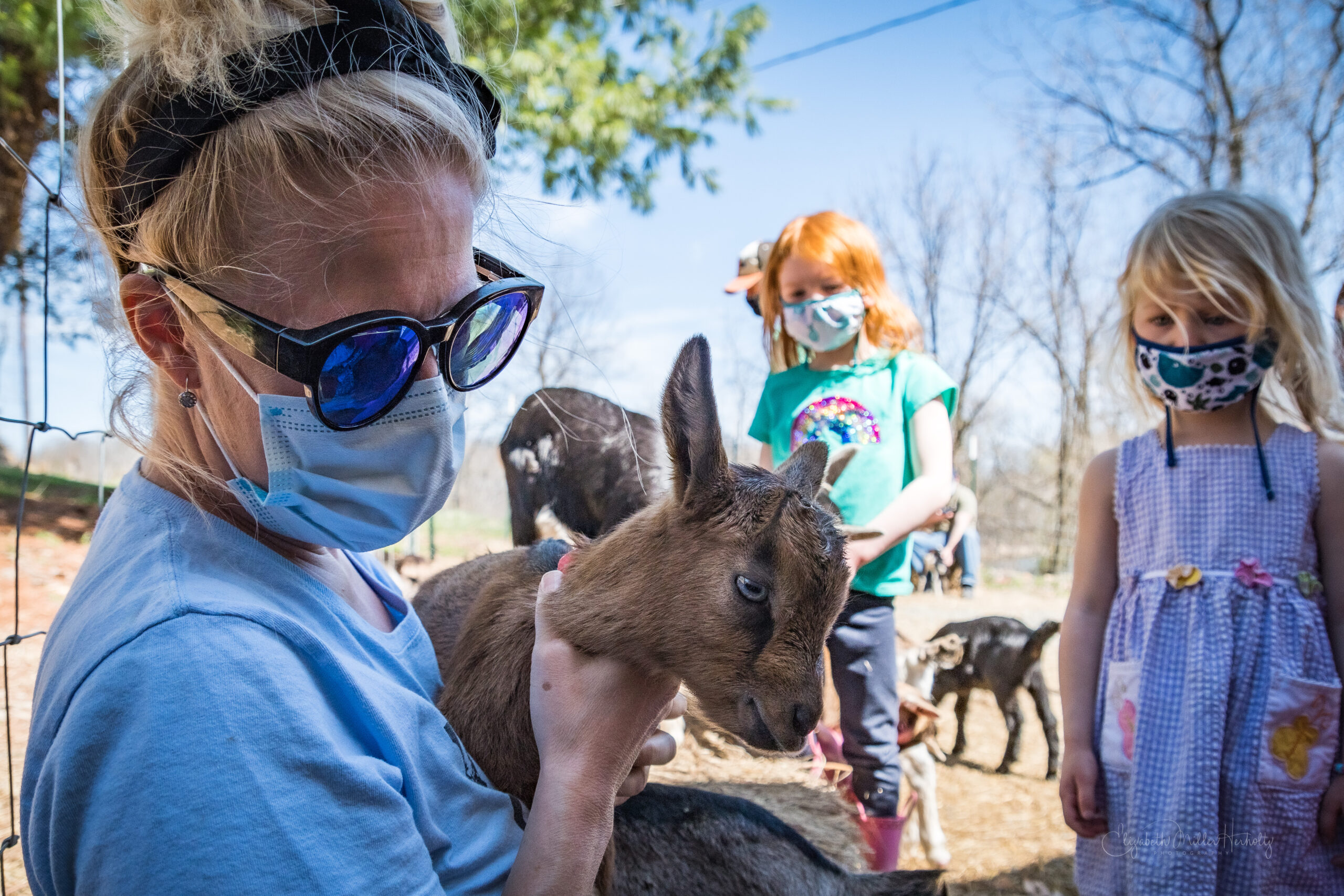 A Woman Holds A Goat As Children Look On.